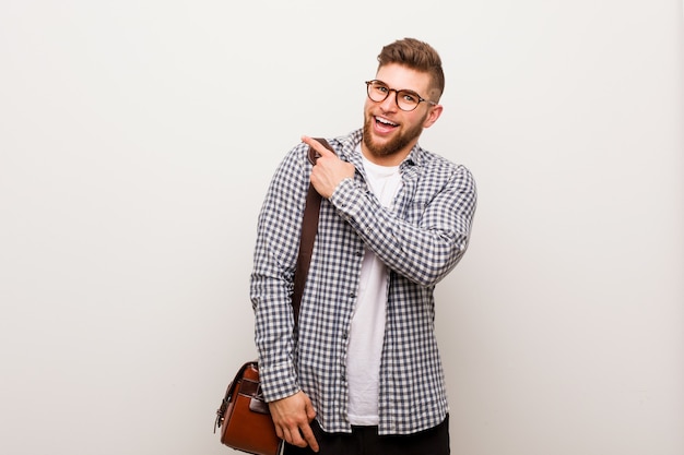 Hombre de negocios moderno joven sonriendo y apuntando a un lado, mostrando algo en el espacio en blanco.