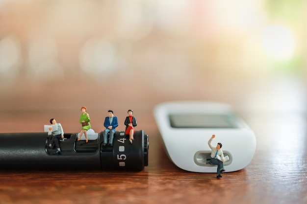 Hombre de negocios y mujer figura de personas en miniatura sentado en lanceta y medidor de glucosa en mesa de madera con espacio de copia.