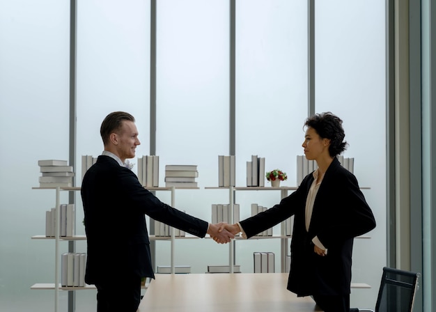 Hombre de negocios y mujer de pie y agitando la mano sobre la mesa en la oficina moderna. éxito del contrato comercial. colaboración entre organizaciones. Capitan del equipo. acuerdo financiero.