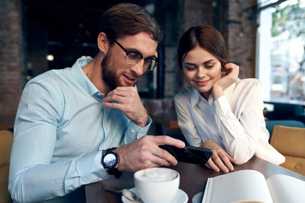 hombre de negocios y mujer sentados en una mesa en un café y mirando el teléfono foto de alta calidad