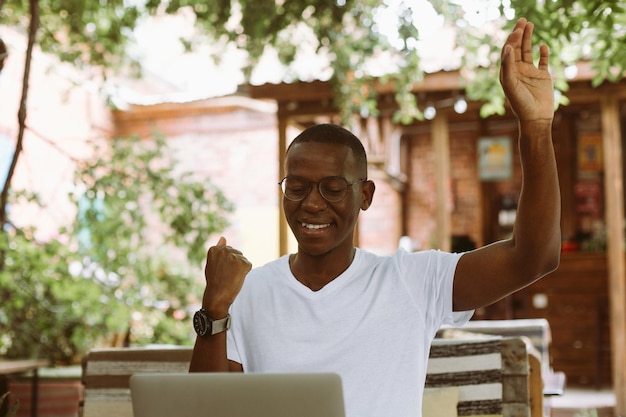 Hombre de negocios multirracial alegre y riendo con gafas trabajando en una computadora portátil levantando el brazo Reunión en línea de videollamada