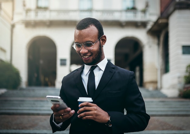 Hombre de negocios negro con celular en mano mira mensajes en la ciudad