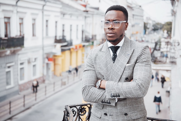 Hombre de negocios negro confidente en un elegante traje de pie en el bloque de oficinas mirando con una expresión seria