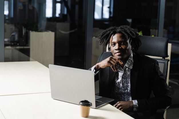 El hombre de negocios negro con laptop está trabajando en línea en la oficina. Un apuesto gerente africano está haciendo trabajo remoto en un espacio de coworking.