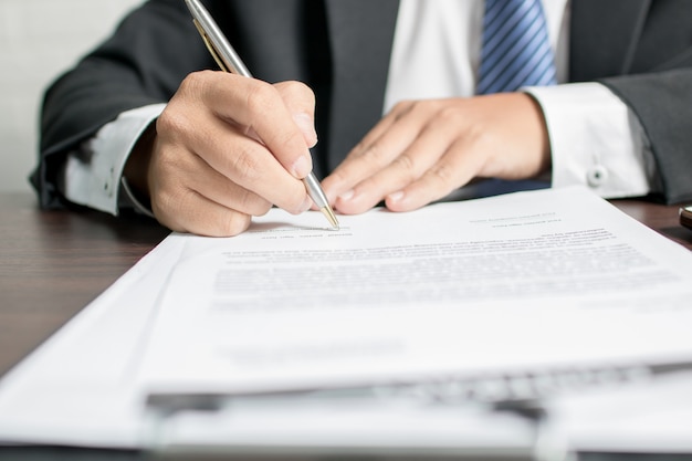Hombre de negocios o abogado que firma en el documento del contrato sobre la tabla en la oficina, concepto como seguro