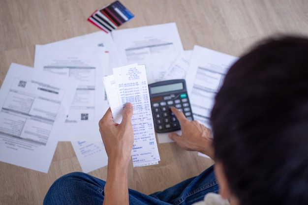 El hombre de negocios o el mayordomo está sentado en la prensa de varias calculadoras de gastos en facturas y deudas de tarjetas de crédito. Los hombres están estresados con la deuda que deben pagar mensualmente. Concepto de deuda