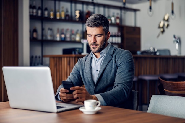 Un hombre de negocios ocupado está sentado en un café agradable y usando su teléfono