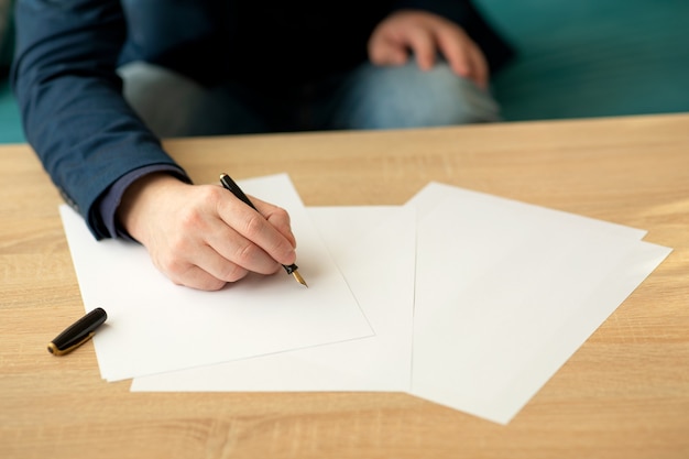 El hombre de negocios en la oficina escribe una carta o firma un documento en una hoja de papel blanco con una pluma estilográfica con plumilla. Primer plano de las manos