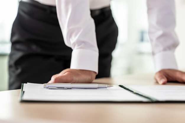 Hombre de negocios con papeleo para firmar delante de él, apoyado en su escritorio de oficina.