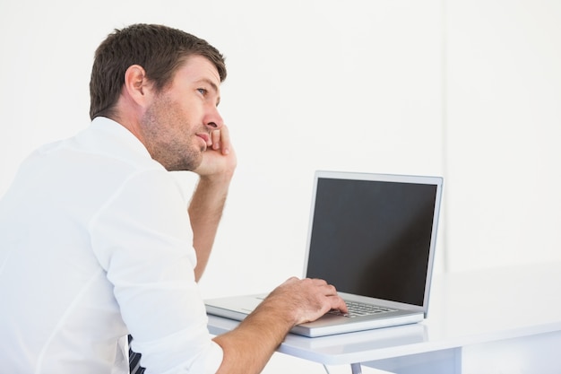 Hombre de negocios de pensamiento sentado en el escritorio usando la computadora portátil