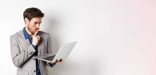 Hombre de negocios pensativo que trabaja en una computadora portátil y piensa mirando pensativo a la pantalla de la computadora de pie