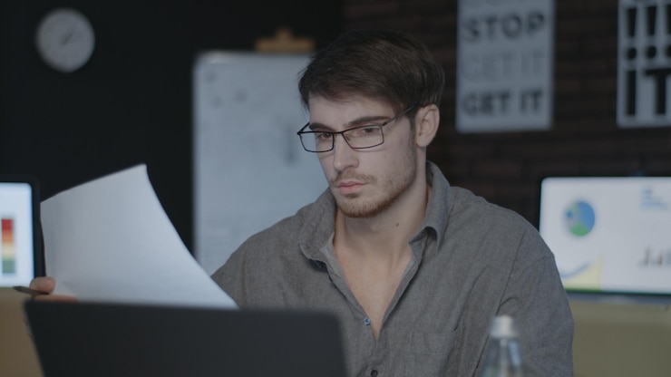 Foto hombre de negocios pensativo que trabaja con documentos cerca de la computadora en la oficina oscura