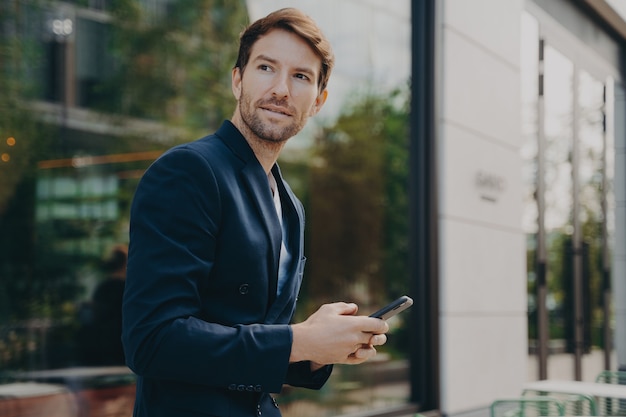 Hombre de negocios pensativo sostiene celular envía mensajes de texto vestido formalmente