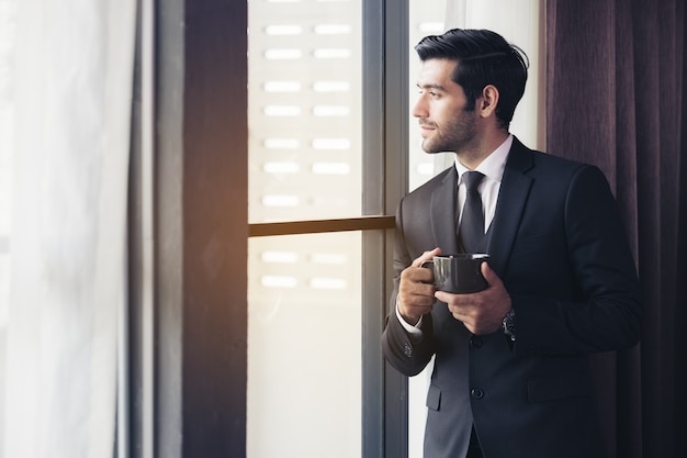 Hombre de negocios pensativo tomando café, mirando por la ventana