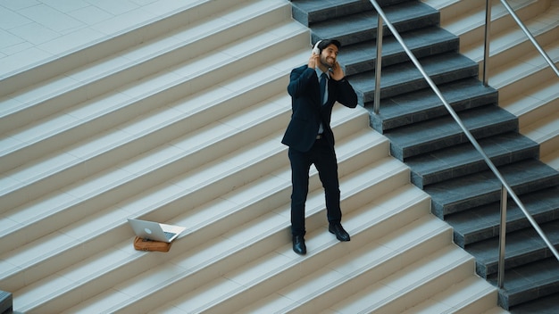 Hombre de negocios de pie en la escalera mientras se mueve a la música de los auriculares exultante