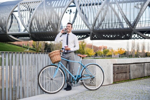 Hombre de negocios de pie junto a su bicicleta vintage hablando por teléfono móvil