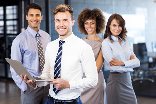 hombre de negocios de pie con un ordenador portátil mientras su equipo de pie detrás de él en la oficina