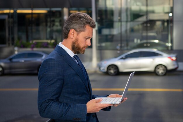 Hombre de negocios con portátil al aire libre Experto en negocios seguro Hombre guapo en traje que sostiene la computadora portátil contra el fondo de la oficina