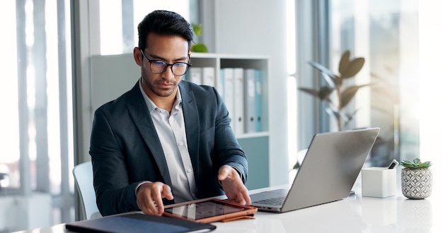 Hombre de negocios portátil y tableta para análisis de datos mercado de valores e investigación en línea para ganancias ventas o cuenta de empresa comerciante asiático inversor o analista en la oficina en tecnología digital y computadora