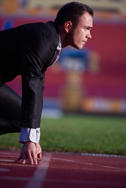 hombre de negocios en posición inicial listo para correr y correr en la pista de carreras de atletismo