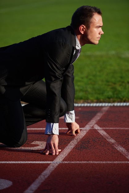 Foto hombre de negocios en posición inicial listo para correr y correr en la pista de carreras de atletismo