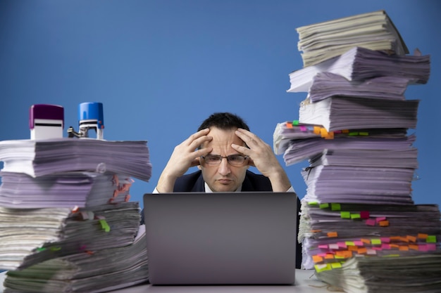 Foto hombre de negocios preocupado cansado sentado en el escritorio de oficina con una enorme pila de documentos