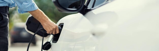 El hombre de negocios progresista de primer plano enchufa el enchufe del cargador de la estación de carga a EV