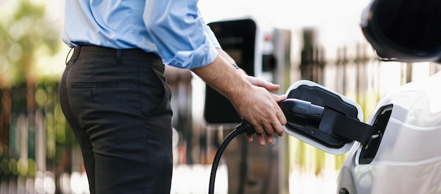 El hombre de negocios progresista de primer plano enchufa el enchufe del cargador de la estación de carga a EV