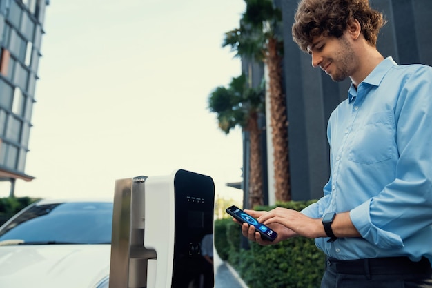 Un hombre de negocios progresista con traje mira el estado de la batería de un vehículo eléctrico desde su teléfono