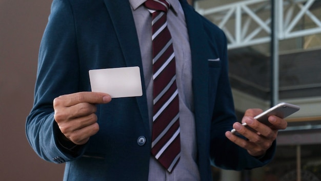Hombre de negocios que muestra la tarjeta de visita en blanco y la celebración de teléfono inteligente.