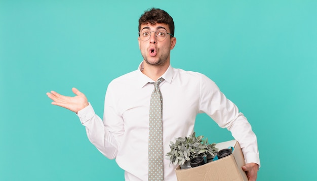 Hombre de negocios que parece sorprendido y consternado, con la mandíbula caída sosteniendo un objeto con una mano abierta en el costado. concepto de despido