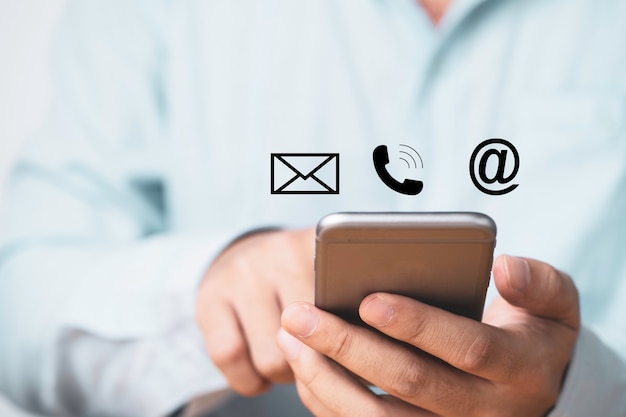 El hombre de negocios que sostiene el teléfono inteligente con iconos de contacto comercial incluye teléfono de correo y dirección para el concepto de servicio al cliente.