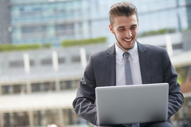 Hombre de negocios que trabaja con la computadora portátil fuera del edificio de oficinas