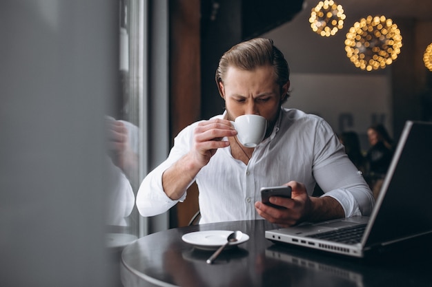 Hombre de negocios que trabaja con la computadora portátil y tomando café en una cafetería