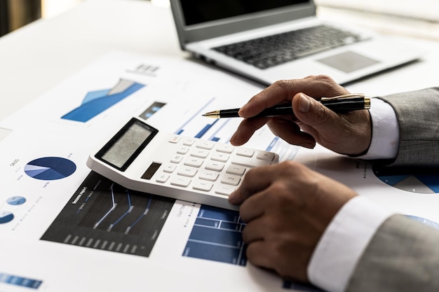 Hombre de negocios que usa una calculadora para calcular números en los documentos financieros de una empresa, está analizando datos financieros históricos para planificar cómo hacer crecer la empresa. Concepto financiero.
