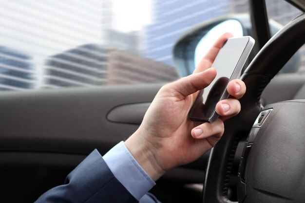 El hombre de negocios que usa un teléfono inteligente móvil mientras conduce el automóvil