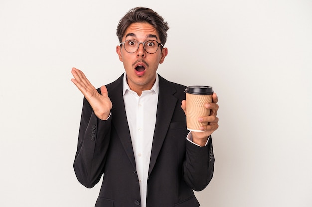 Hombre de negocios de raza mixta joven sosteniendo café para llevar aislado sobre fondo blanco sorprendido y conmocionado.