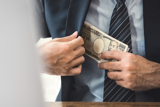 Hombre de negocios rico manteniendo el dinero del billete de Yen japonés en el bolsillo de su traje