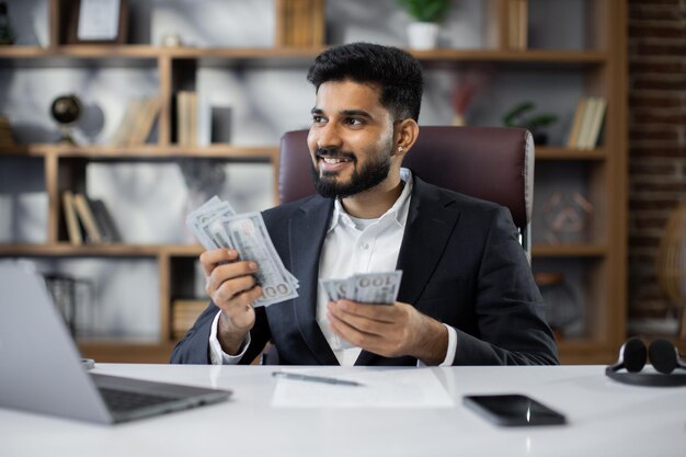 Un hombre de negocios rico que trabaja en una computadora portátil contando dinero en efectivo calcula las ganancias