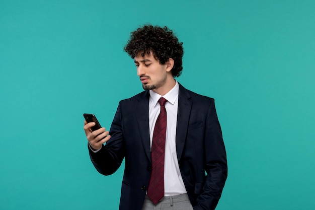 Hombre de negocios rizado lindo chico guapo en traje negro y corbata roja mirando una pantalla de teléfono