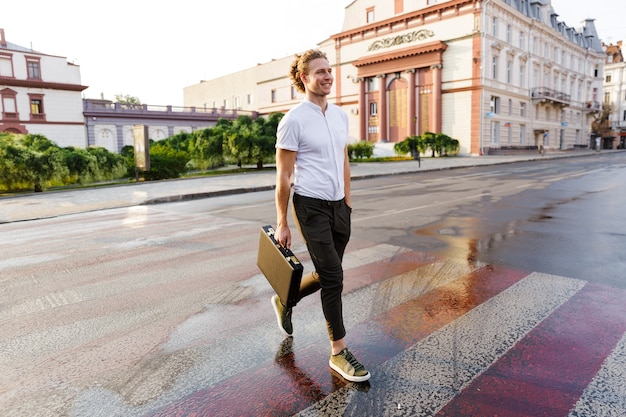 Hombre de negocios rizado sonriente con maletín caminando por la calle