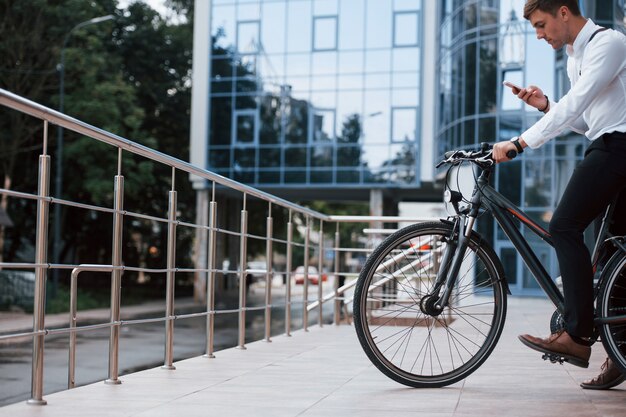 Foto hombre de negocios en ropa formal con bicicleta negra está en la ciudad.