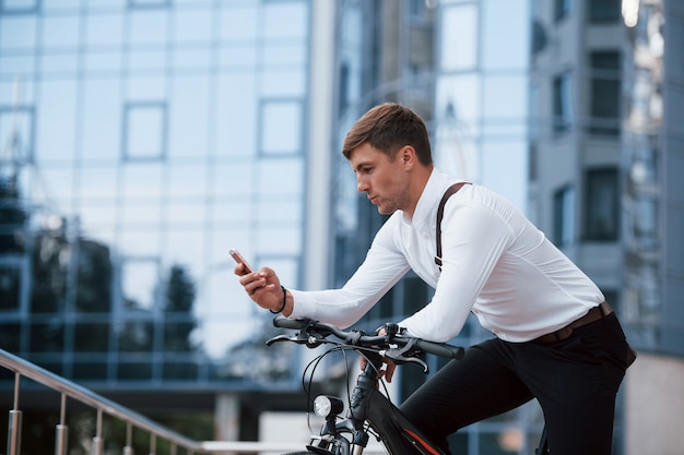 Hombre de negocios en ropa formal con bicicleta negra está en la ciudad.