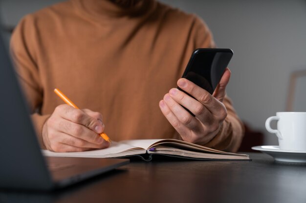 Foto el hombre de negocios con ropa informal está sentado sosteniendo un teléfono inteligente tomando notas