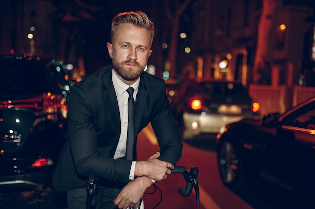 Hombre de negocios seguro con bicicleta en la carretera de la ciudad de noche