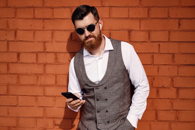 Foto hombre de negocios seguro de carácter permanente en traje con teléfono móvil y auriculares inalámbricos