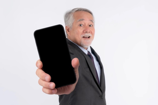 Hombre de negocios senior asiático anciano con traje se siente feliz señalando con el dedo a un gran teléfono inteligente con pantalla en blanco pantalla negra aislada en fondo blanco pantalla vacía de teléfono inteligente Imagen de maqueta