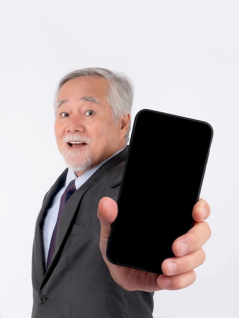 Hombre de negocios senior asiático anciano con traje se siente feliz señalando con el dedo a un gran teléfono inteligente con pantalla en blanco pantalla negra aislada en fondo blanco pantalla vacía de teléfono inteligente Imagen de maqueta