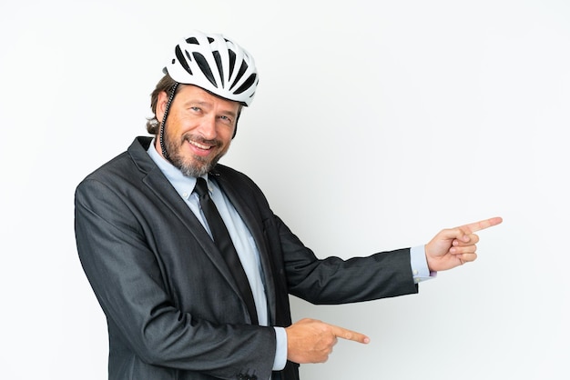 Hombre de negocios senior con un casco de bicicleta aislado sobre fondo blanco apuntando con el dedo hacia el lado y presentando un producto
