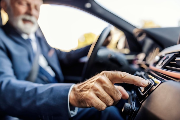 El hombre de negocios senior está sentado en su auto y presionando el botón